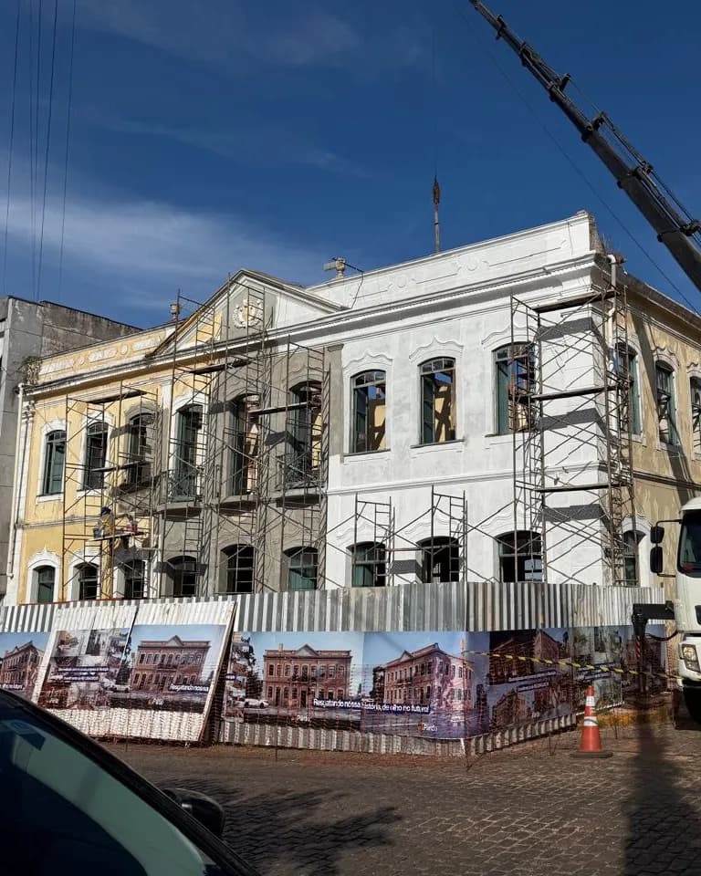 Restauro de prédio histórico em andamento, com fachada em recuperação, andaimes e guindaste posicionado na obra