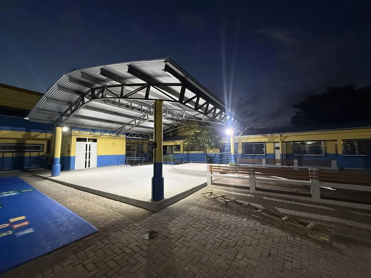 Área externa concluída com cobertura metálica, iluminação e circulação pavimentada